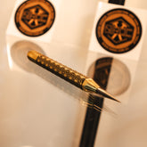 A gold and black patterned scribe lies on a reflective surface, made out of brass and carbide