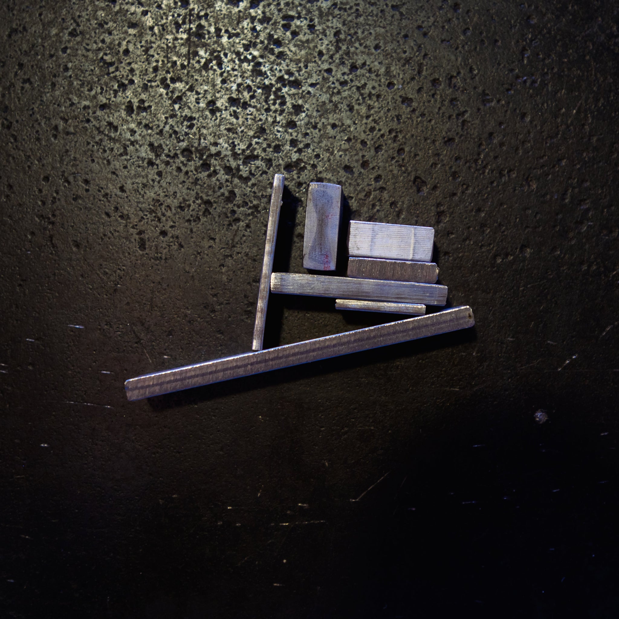 different size Stainless Steel Flat bar pieces arranged and photographed on a dark textured surface under direct light.