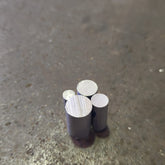 Four small cylindrical ally rods with silver-colored circular ends, standing upright on a textured steel bench.
