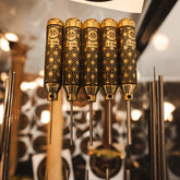 Five polished brass pin punches with intricate geometric engravings, displayed vertically in a rack with a blurred workshop background and a Niroc logo visible at the top.