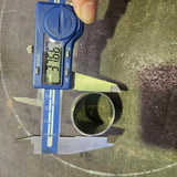 A blue digital caliper measuring the diameter of a small metal tube, with a finger holding the caliper at the top and the display reading 38.1 mm.