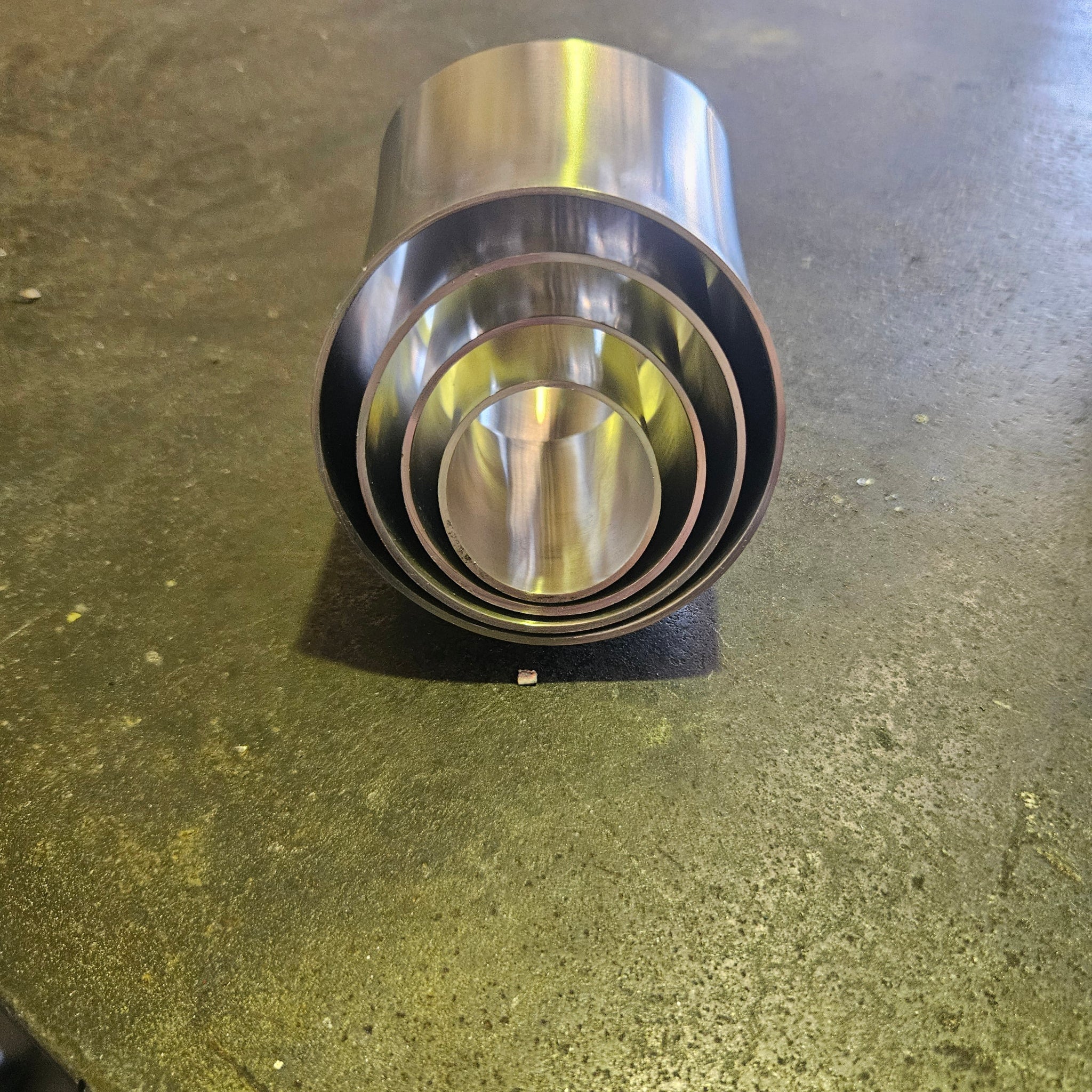 A set of nested stainless steel 45 degree tube bends, photographed on a textured steel bench.