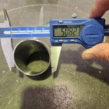 A digital caliper measuring the outer diameter of a metal tube, with a hand holding the calliper. The caliper has a blue display screen reading 50.8mm and silver metal jaws, and the tube is positioned on a dark, textured surface.