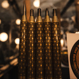 Five decorative blackened and polished brass precision scribe and punch set with intricate geometric patterns on their handles, arranged upright in a row against a warm, blurred background.