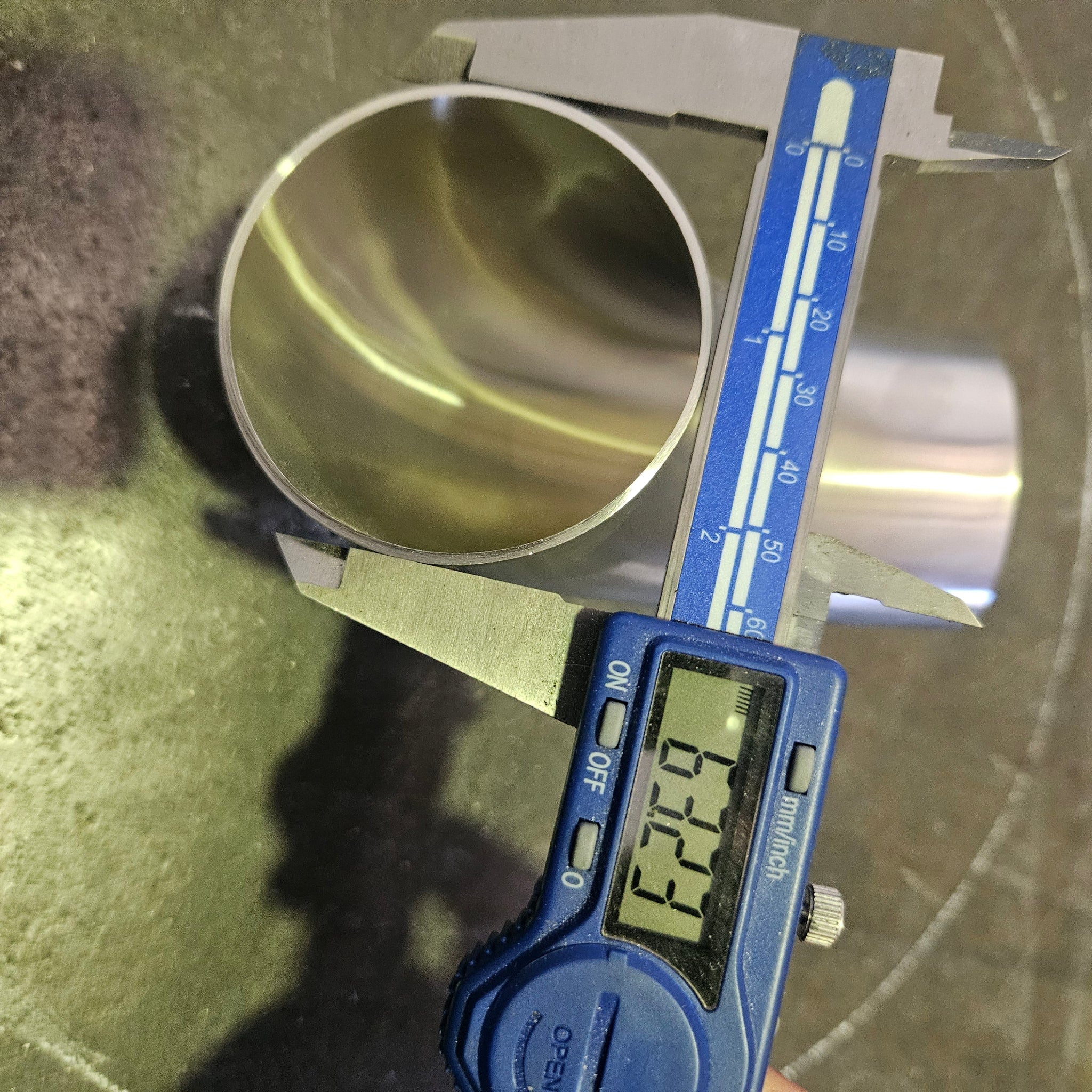 A digital caliper measuring the diameter of a polished metal cylinder, with the caliper displaying 63.5mm.