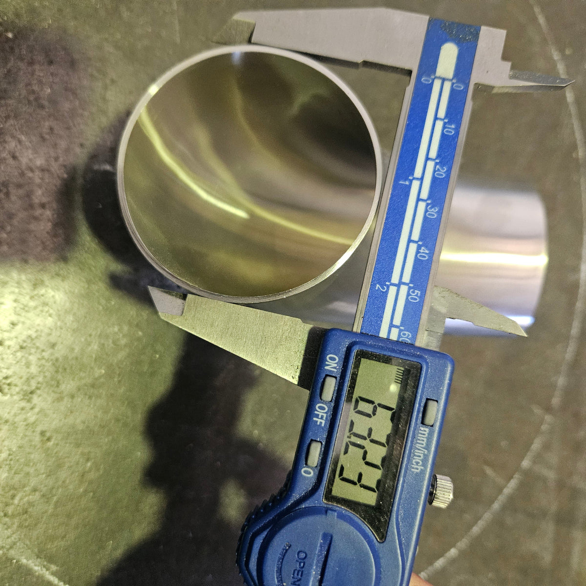 A digital caliper measuring the diameter of a polished metal cylinder, with the caliper displaying 63.5mm.