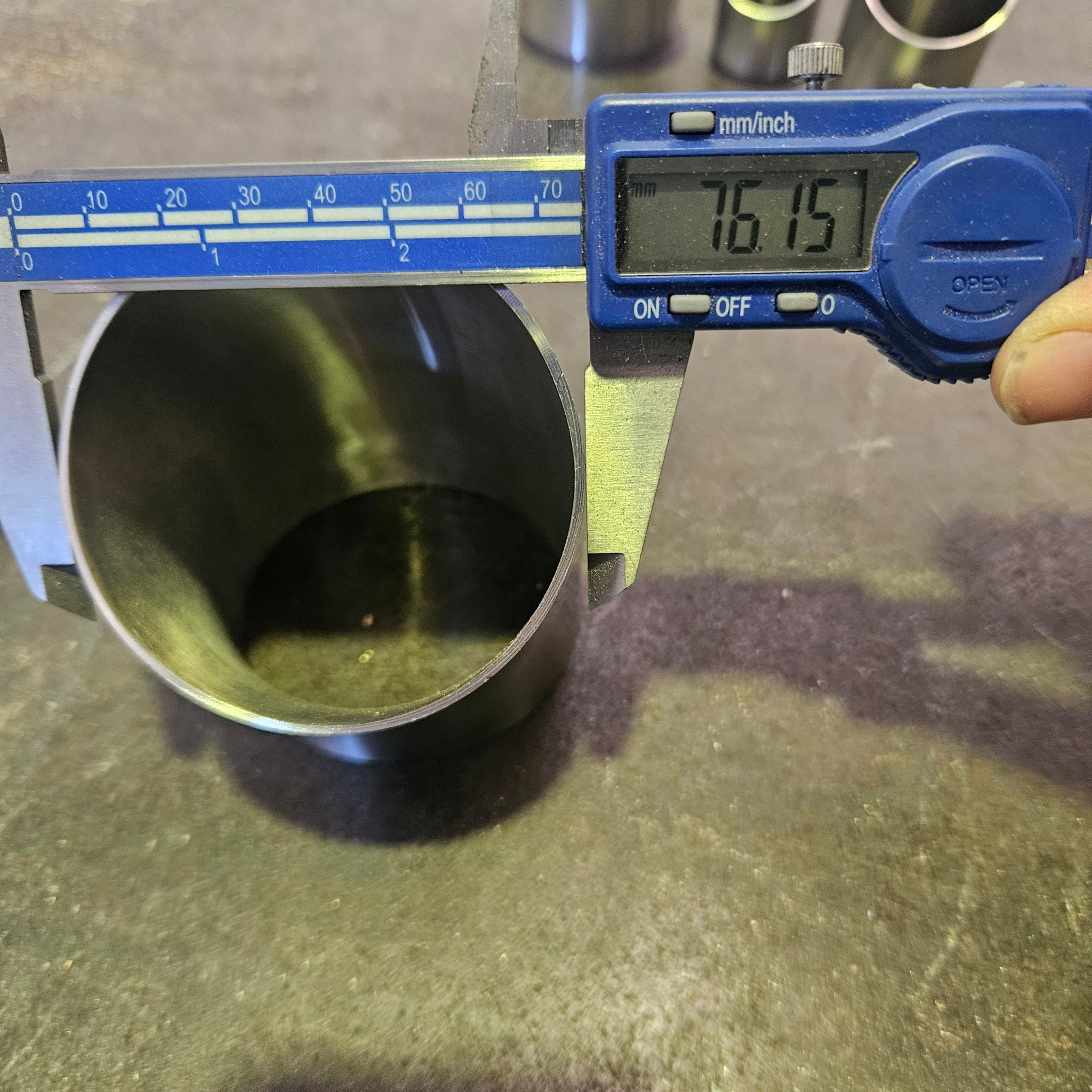 a stainless steel 45 degree bend being measured with a blue set of calipers that reads 76.2mm