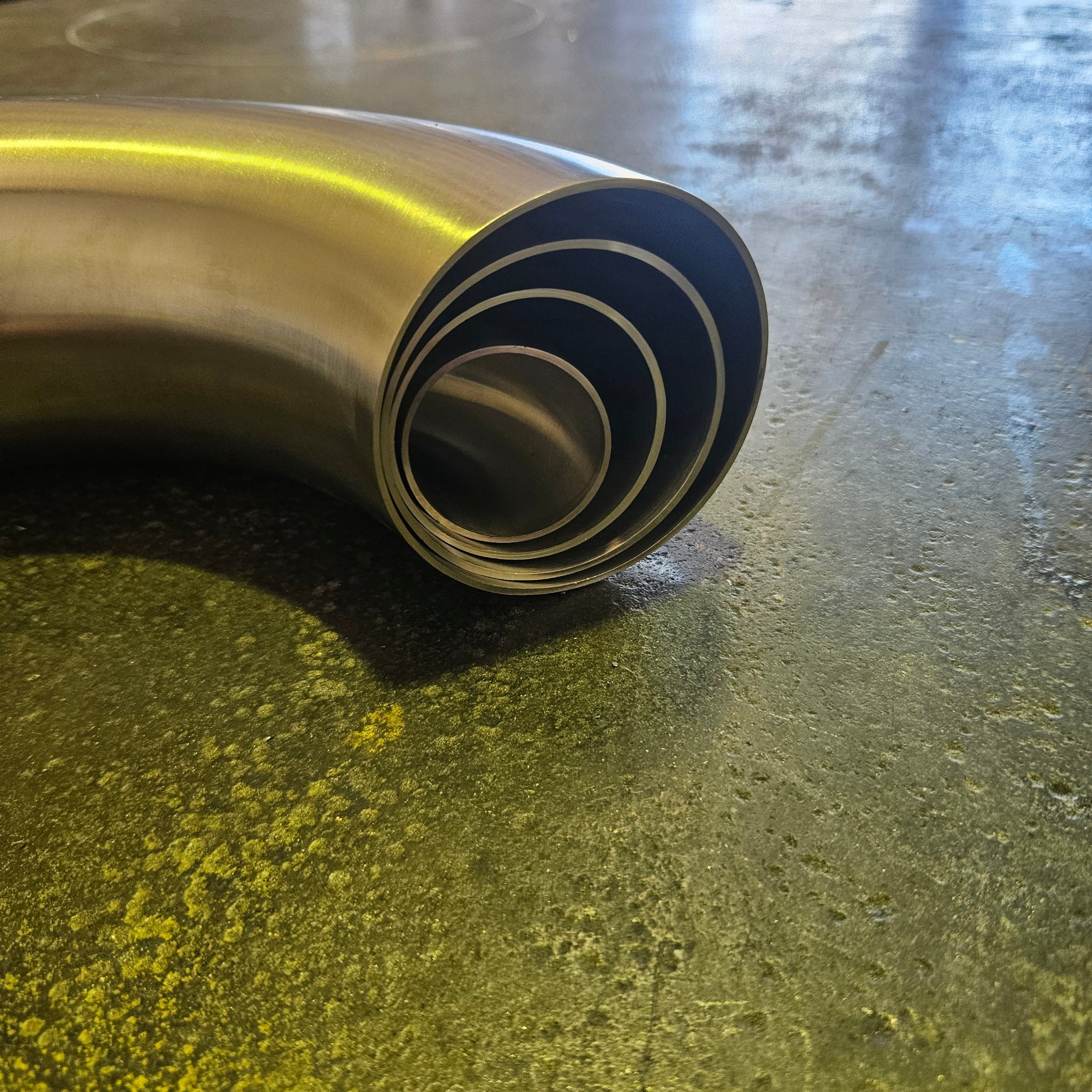 A close-up of a curved stainless steel exhaust tube bends resting on a steel bench.