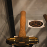 A brass and wood hammer displayed on a glass shelf.