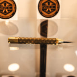 A gold and black patterned precision scribing tool, made out of brass and carbide resting on a reflective surface.