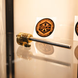 A brass and stainless steel marking gauge, displayed on a glass shelf with a warm beige background and circular stickers.