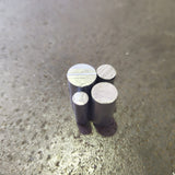 Four small cylindrical aluminium rods of different heights standing upright on a textured steel bench.