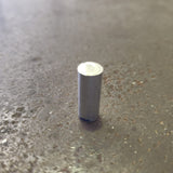 A small cylindrical metal object with a silver top and a dark gray body, standing upright on a textured steel bench.