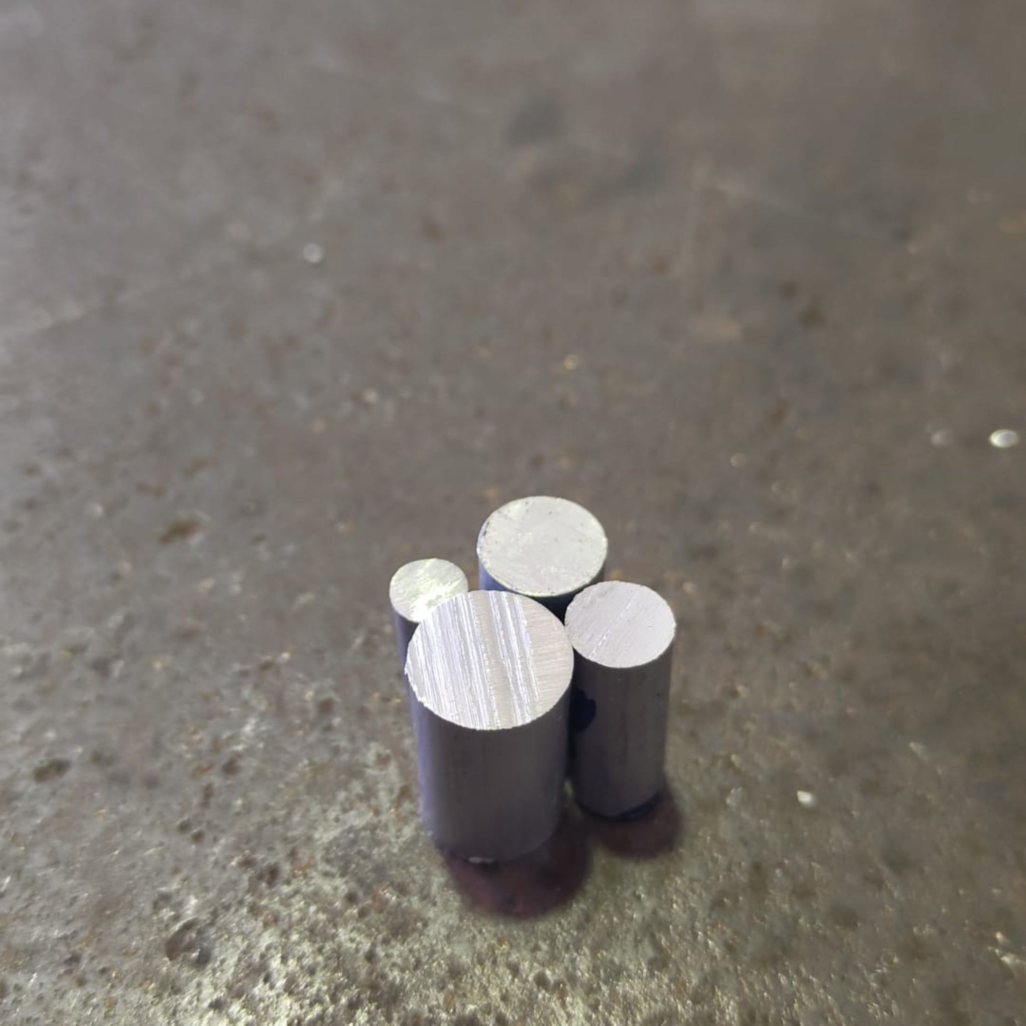 Four small cylindrical ally rods with silver-colored circular ends, standing upright on a textured steel bench.