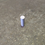 A small cylindrical aluminium rod or pin with a silver top, standing upright on a textured gray surface.