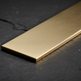 A close-up of a rectangular brushed gold metal bar resting diagonally on a dark textured stone surface.