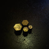 Four small hexagonal brass pieces with a brushed gold finish, arranged in a cluster on a dark, textured surface.
