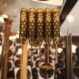 Five polished brass pin punches with intricate geometric engravings, displayed vertically in a rack with a blurred workshop background and a Niroc logo visible at the top.