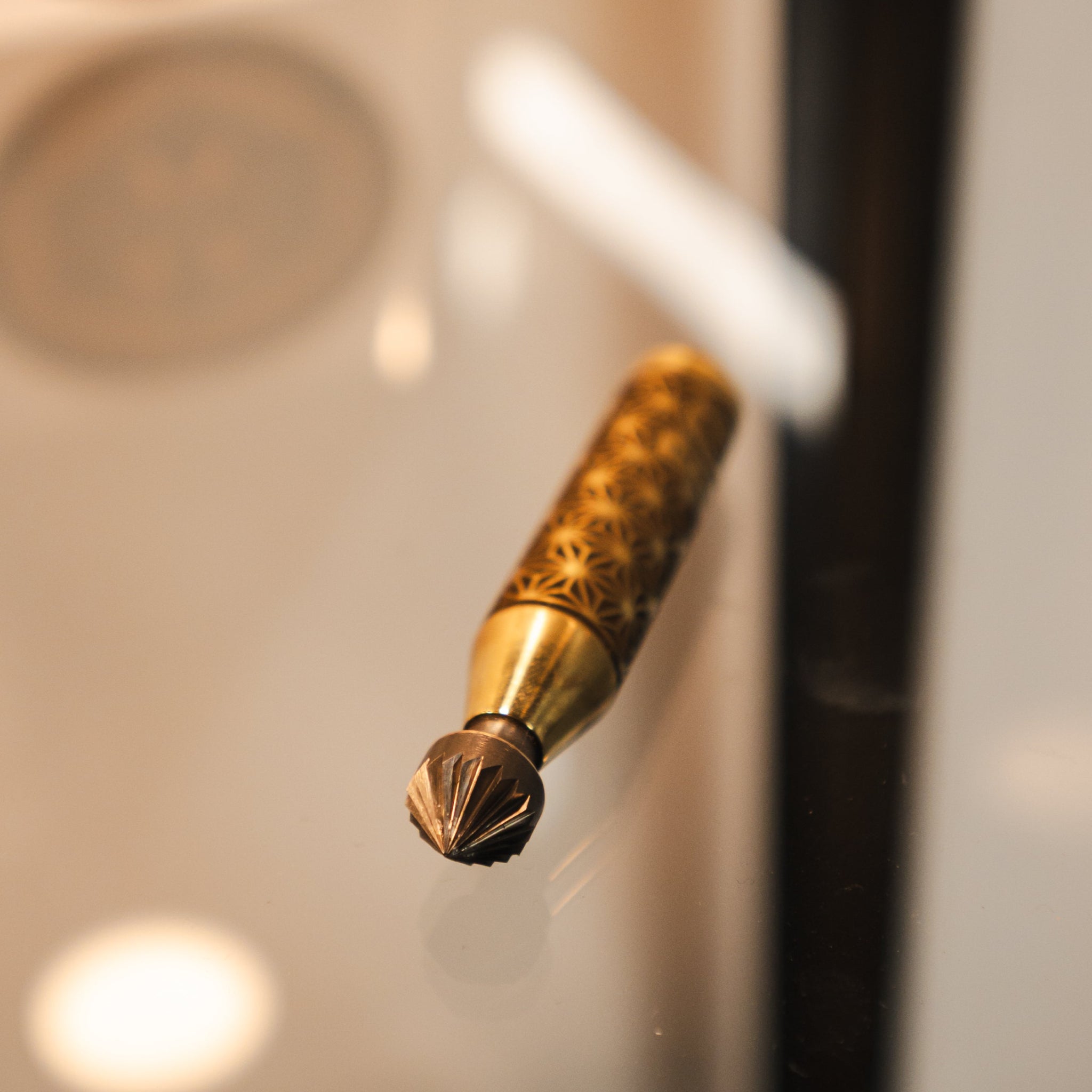 A close-up of a luxury gold-toned deburring tool with an ornate patterned handle, resting on a reflective surface.