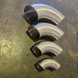 Four curved stainless steel exhaust tips of varying sizes arranged vertically on a textured, dark metallic surface.