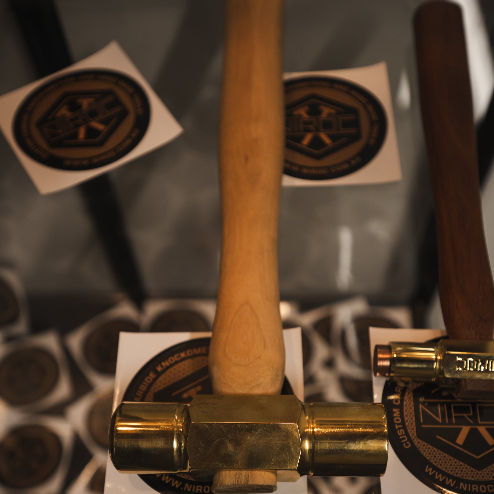 Close-up of a hammer with a light wood handle and brass head resting on a reflective surface