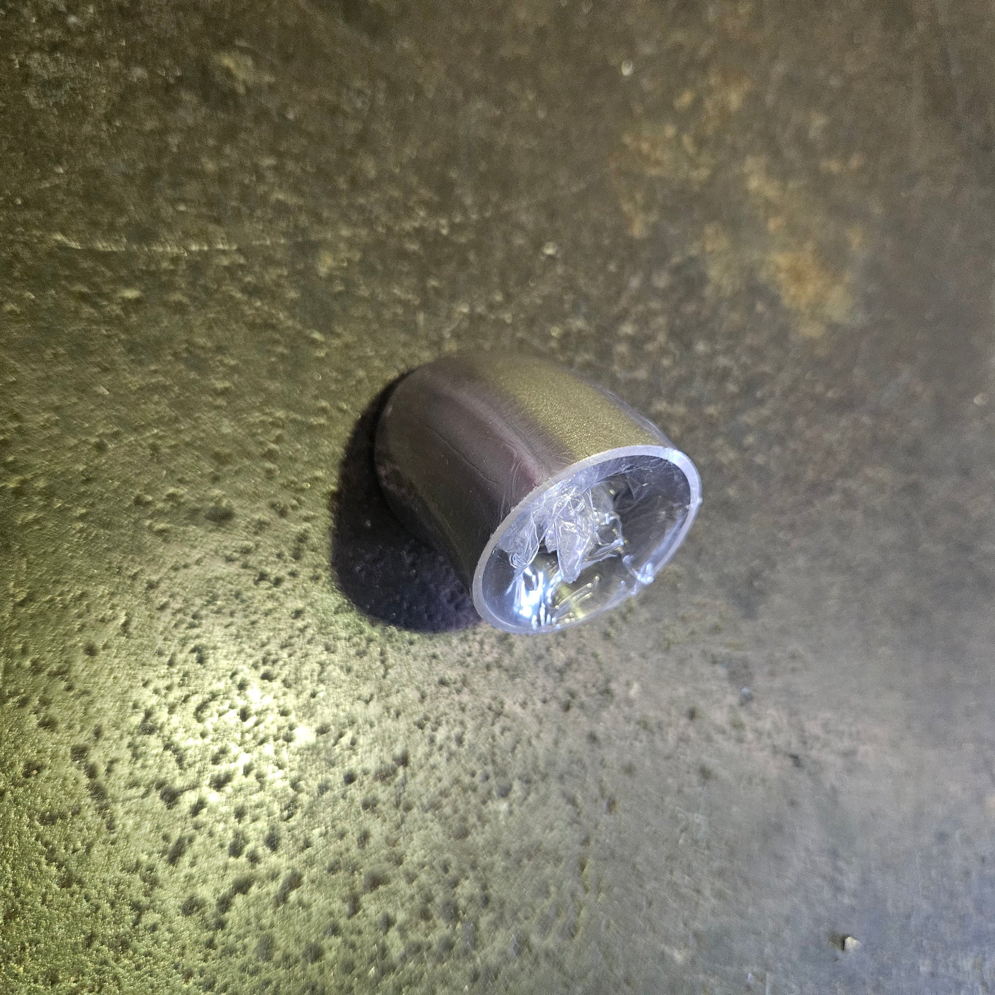 A stainless tube bend wrapped in clear plastic for protection, lying on a textured steel bench under direct light.